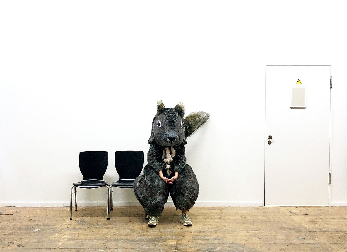 Foto: Person in Grauhörnchen-Kostüm, sitzend auf einem Stuhl