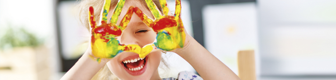 Kind hält Hände mit Fingerfarben vor das Gesicht