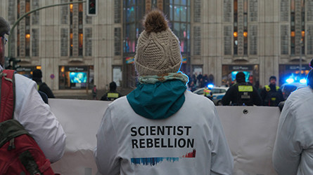 Filmstill aus "Das Gewicht der Welt": Rückenansicht einer Person, auf deren Shirt der Aufdruck "Scientist Rebellion" steht.