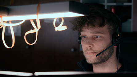 Filmstill aus "Hundertzwölf": konzentriert schauender, junger Mann mit Headphone